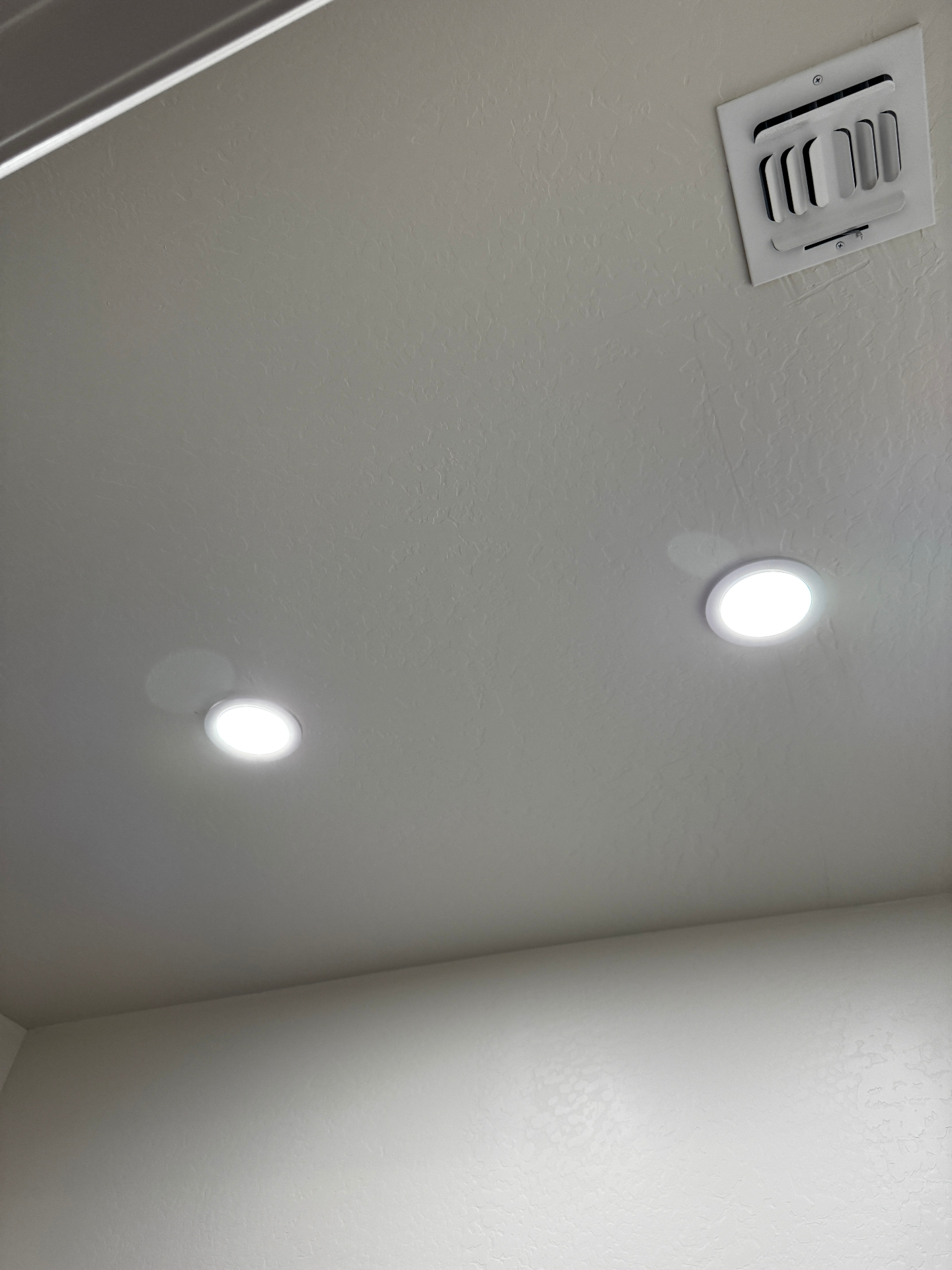 Recessed LED lighting installed in a smooth ceiling next to an HVAC vent in an Arizona home by American Home Pros of Arizona