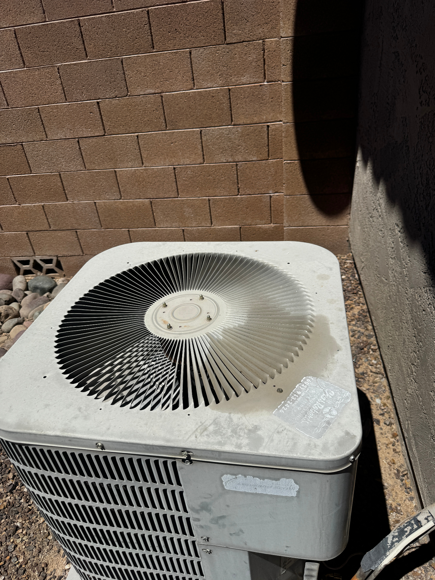 An aging outdoor AC condenser unit beside a brick wall in Arizona — the kind of system often misdiagnosed as needing full replacement.