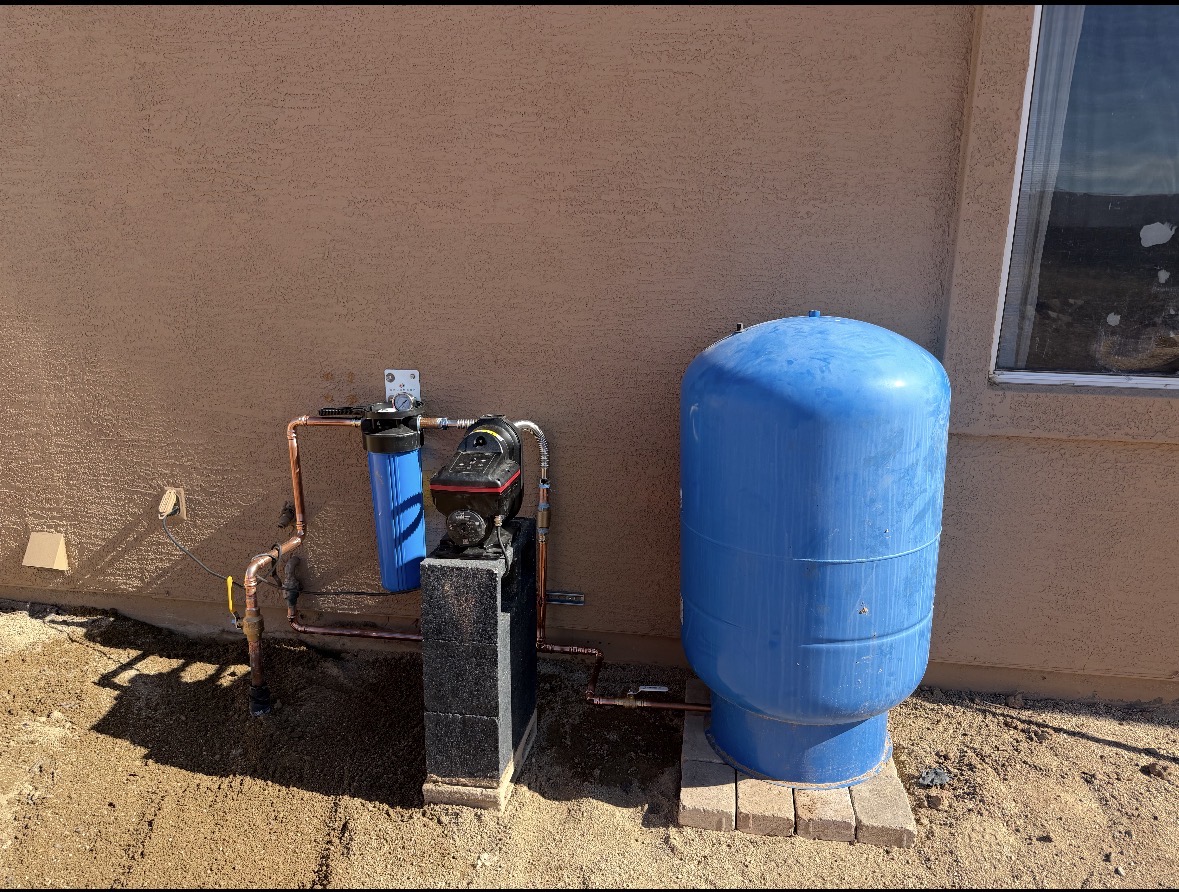 Whole-home water pressure booster pump with filter and pressurized storage tank installed on an Arizona home exterior