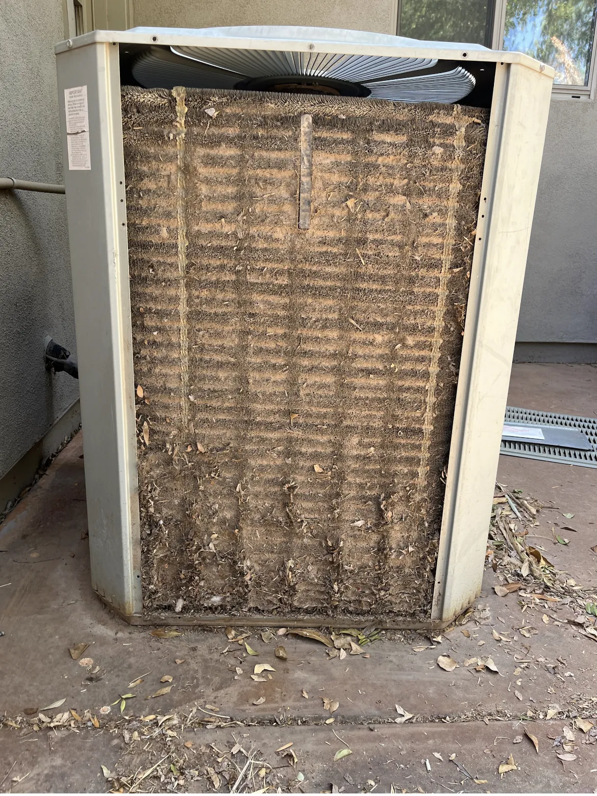 Outdoor condenser unit with heavy debris and dirt buildup across the coil